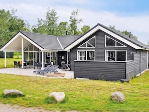 A modern house with a covered patio, outdoor seating, and a grassy yard. - 5 Star Holiday Home in Vaeggerlose (Vaeggerlose)