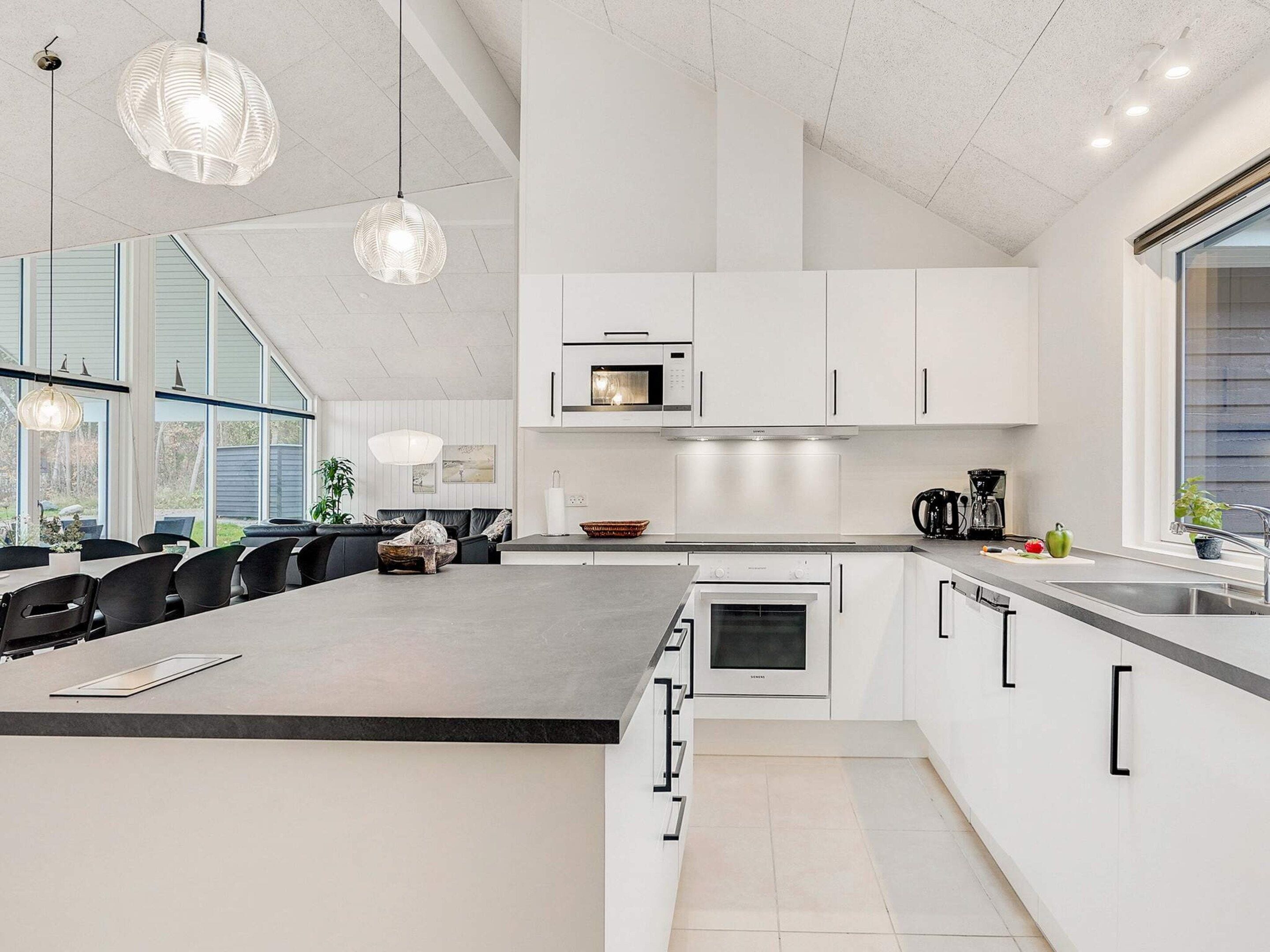 Une cuisine moderne avec des meubles blancs, un grand îlot central et un coin repas doté de chaises noires.