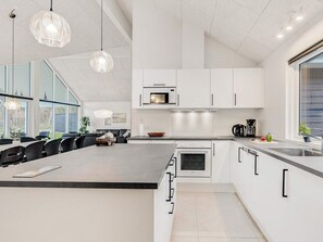 A modern kitchen with white cabinetry, a large island, and a dining area with black chairs. - 5 Star Holiday Home in Vaeggerlose (Vaeggerlose)