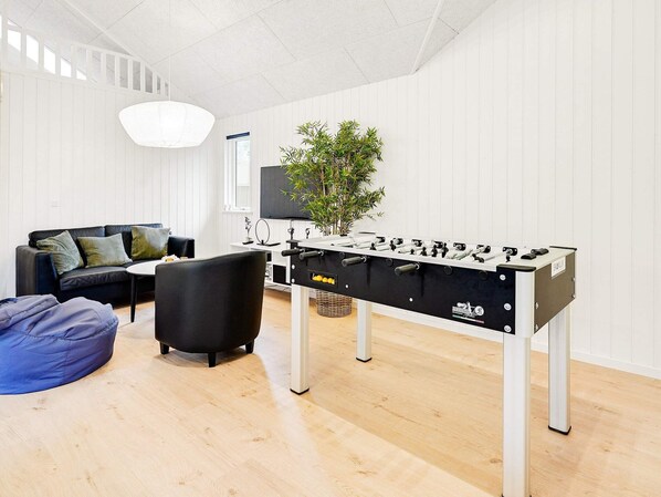 Un salon moderne avec un baby-foot, un canapé, une table basse et une plante en pot.