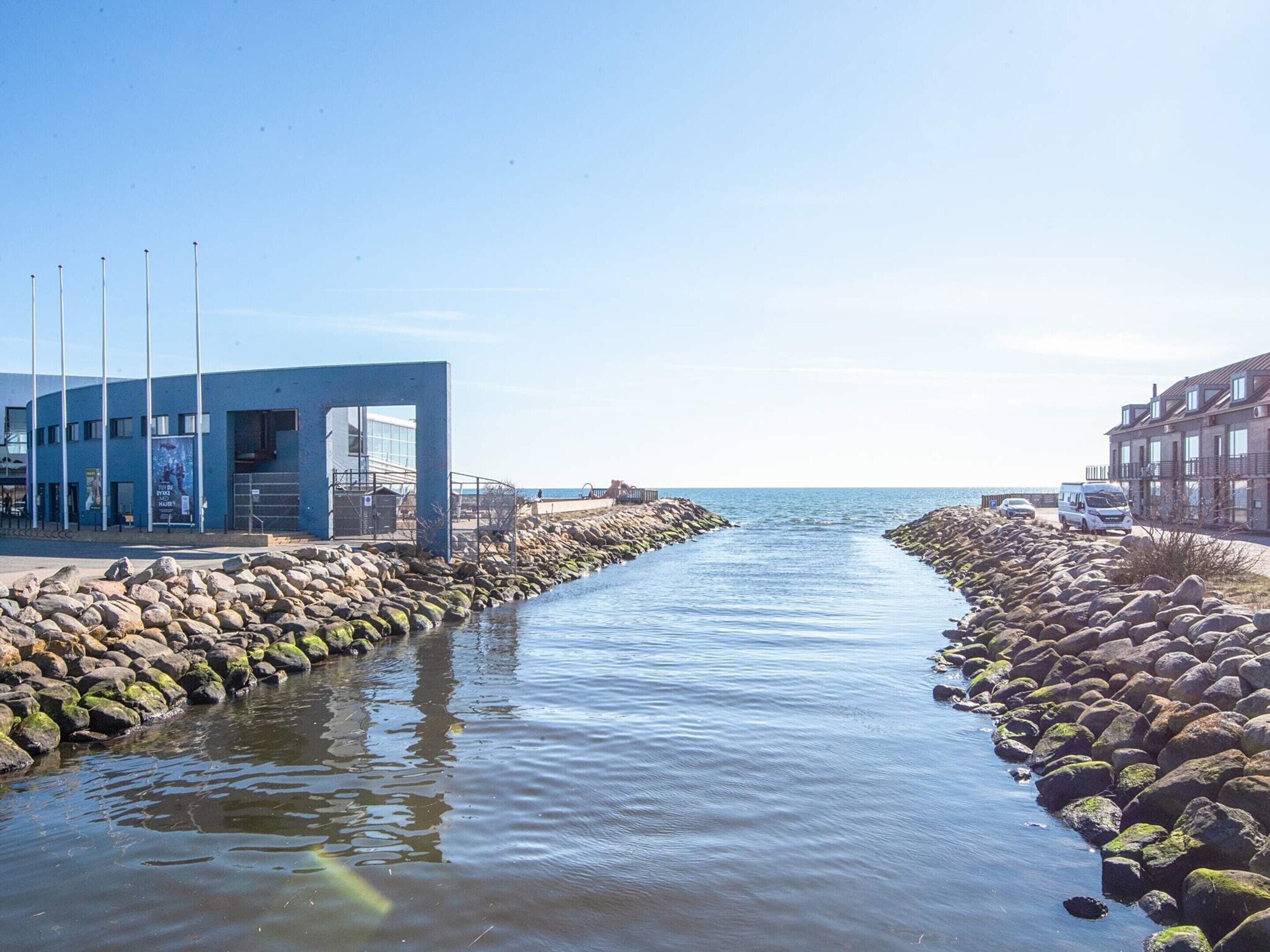 A coastal walkway with a blue building, a rocky shoreline, and a clear view of the sea.