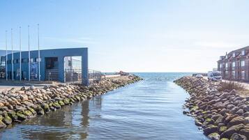 A coastal walkway with a blue building, a rocky shoreline, and a clear view of the sea.