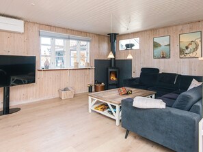A cozy living room with a sofa, a flat-screen TV, a fireplace, and wooden walls.