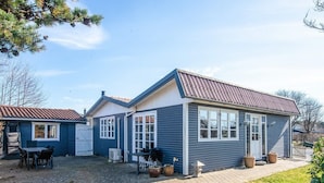 Uma casa de dois andares com calçada pavimentada, varanda coberta com mobiliário exterior e um pequeno jardim.