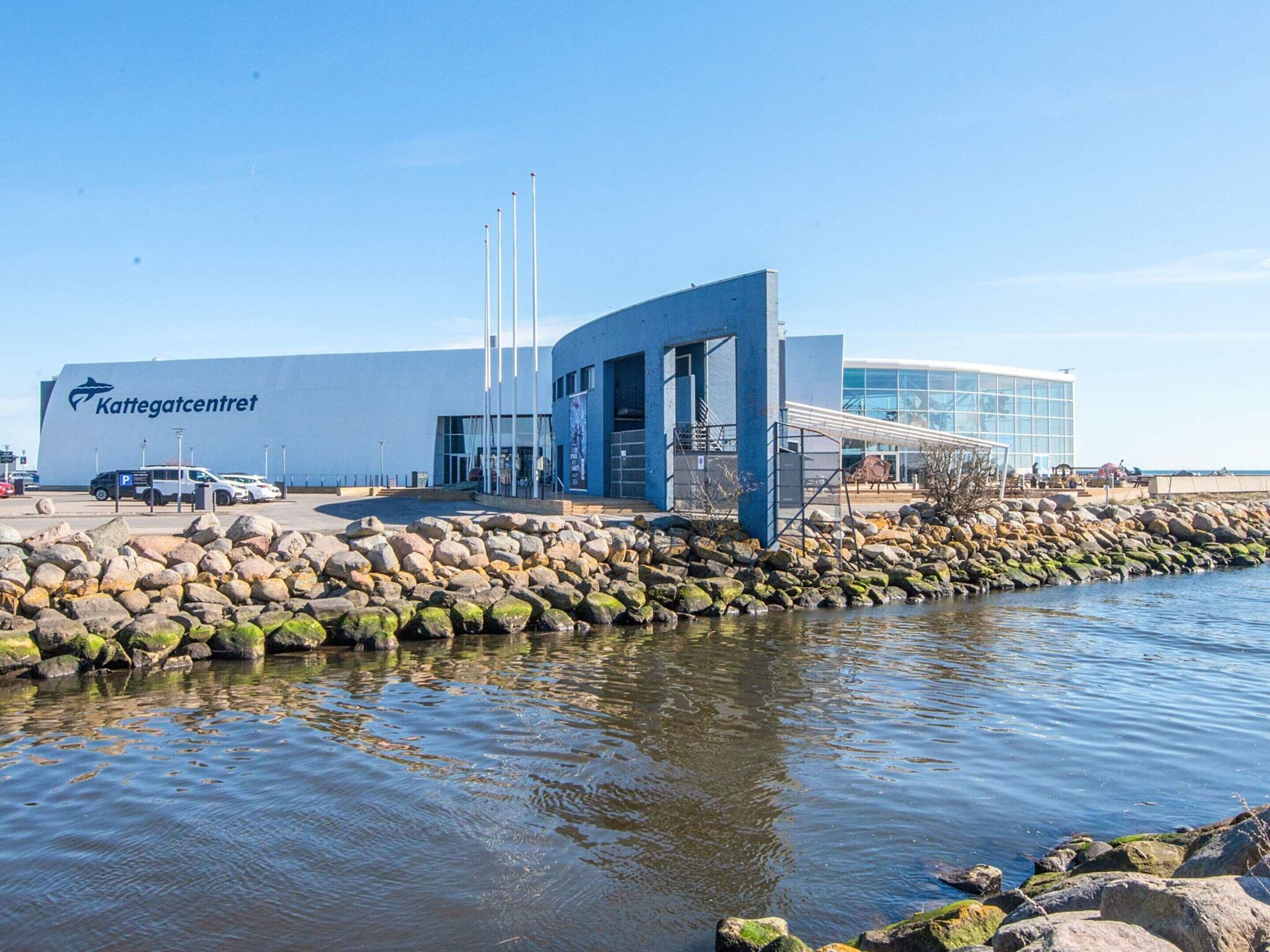A modern building with a large sign reading 'Kattegatcentrum,' a parking area, and a rocky shoreline.