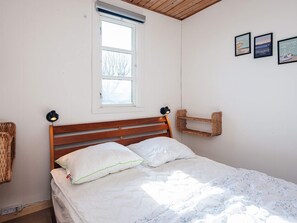 A bedroom with a wooden bed, white bedding, a window, and wall-mounted pictures. - 4 Star Holiday Home in Grenaa (Grenaa)