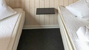Una habitación pequeña y acogedora con dos camas, una mesita de noche y una lámpara de pared.