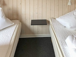 A small, cozy room with two beds, a nightstand, and a wall-mounted lamp.