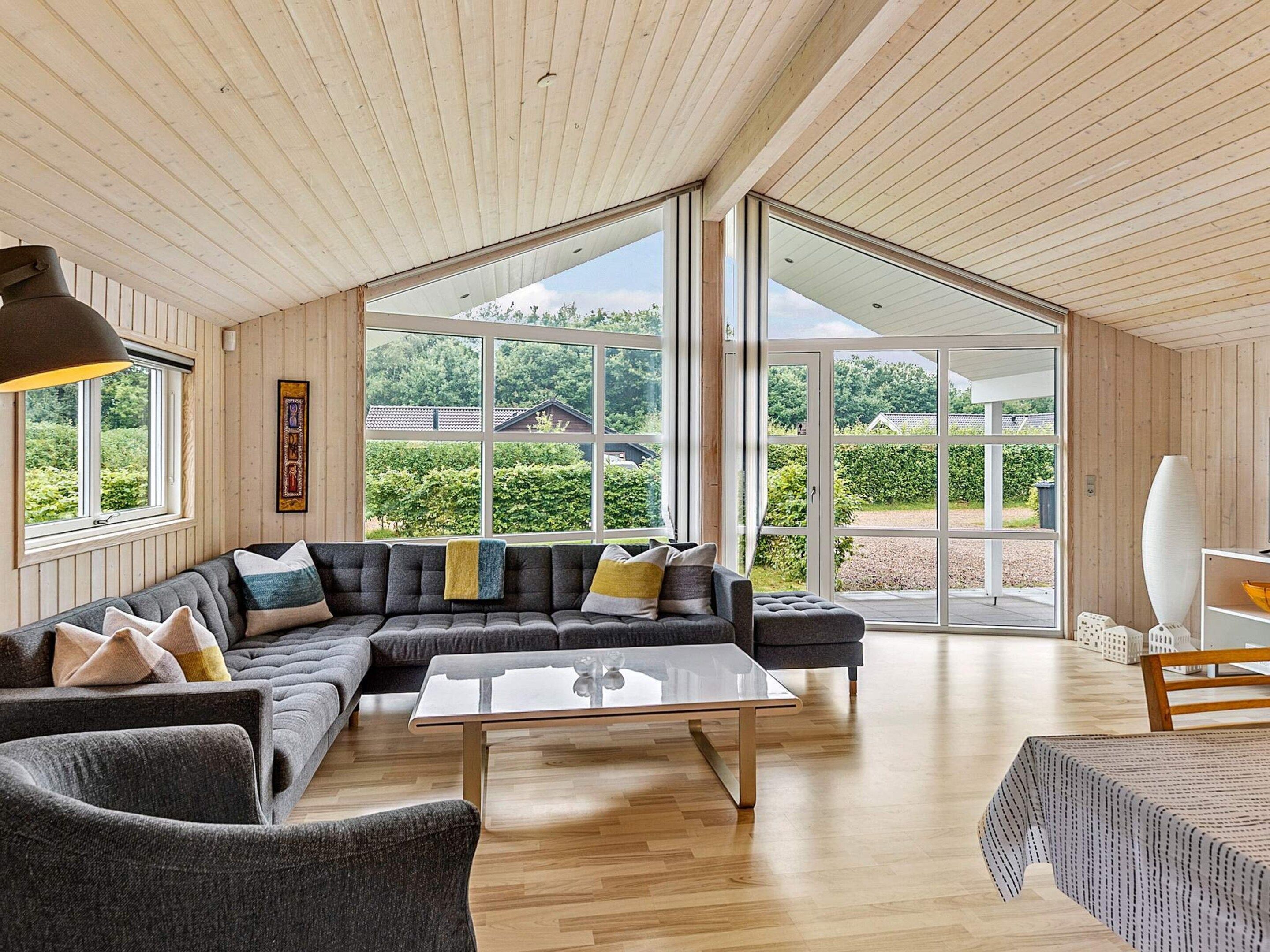 Un salon moderne avec un canapé d’angle, une table basse en verre et de grandes fenêtres donnant sur l’extérieur.