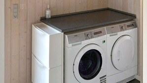 Una unidad compacta de lavadora y secadora con un panel de control, un pequeño estante encima y un cuadro eléctrico en la pared.