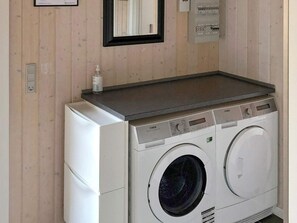 A compact washer and dryer unit with a control panel, a small shelf above it, and a wall-mounted electrical panel.