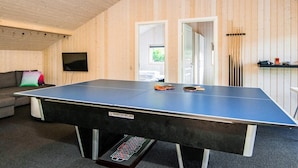 A ping pong table with a label, a sofa with cushions, a television, and a door leading to another room.