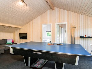 Ett bordtennisbord med en etikett, en soffa med kuddar, en tv och en dörr som leder till ett annat rum.
