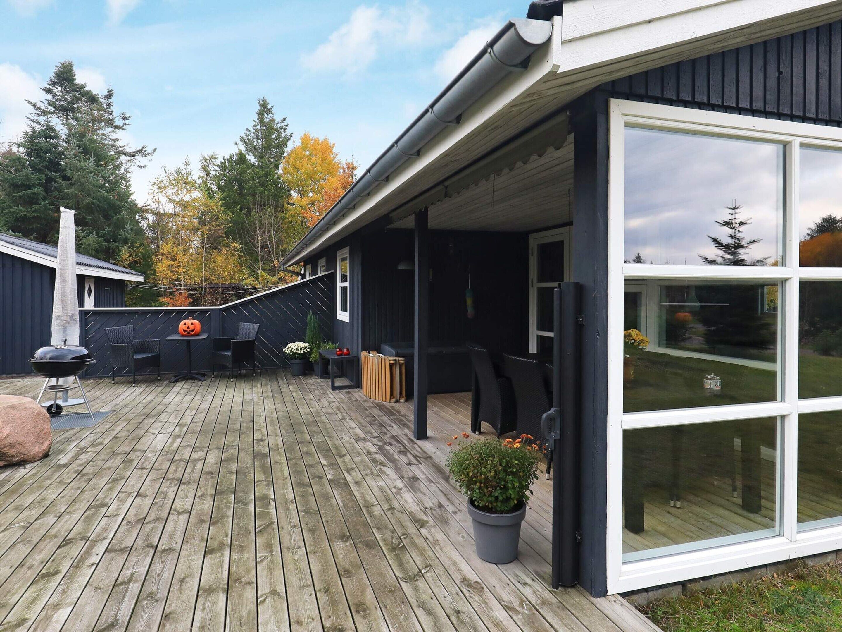 Une terrasse en bois avec des meubles d’extérieur, un barbecue et une plante en pot.