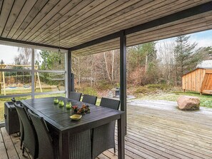 A covered outdoor dining area with a table and chairs, large windows, and a view of a backyard with a swing set. - 6 Person Holiday Home in Hals (Hals)