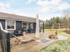 Um deck de madeira com móveis de exterior, baloiço e pérgola.
