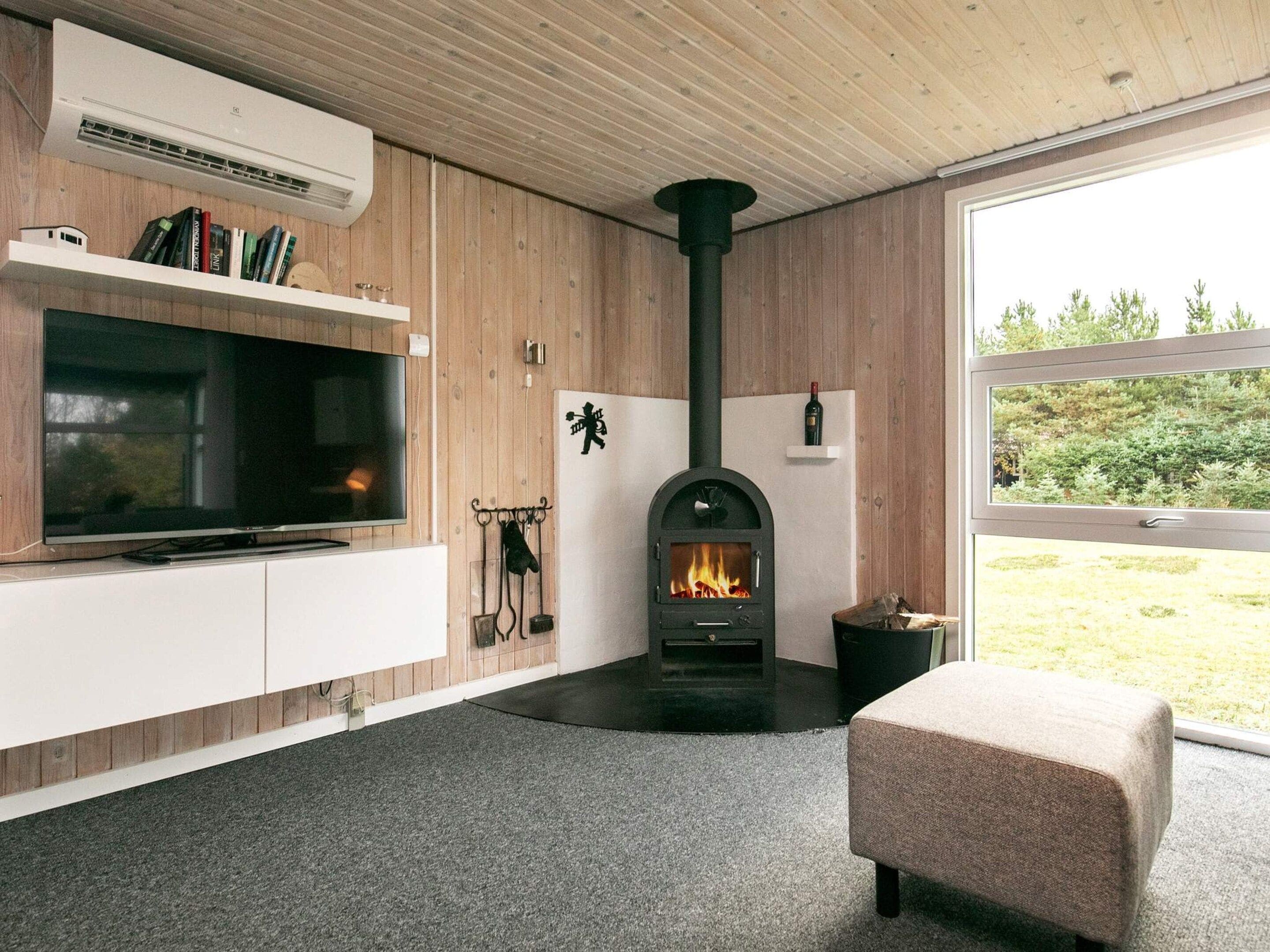 Un salon moderne avec une cheminée, un téléviseur et une fenêtre donnant sur un paysage verdoyant.