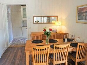 Un área de comedor con una mesa de madera y sillas, un florero con flores, una lámpara y un cuadro en la pared.