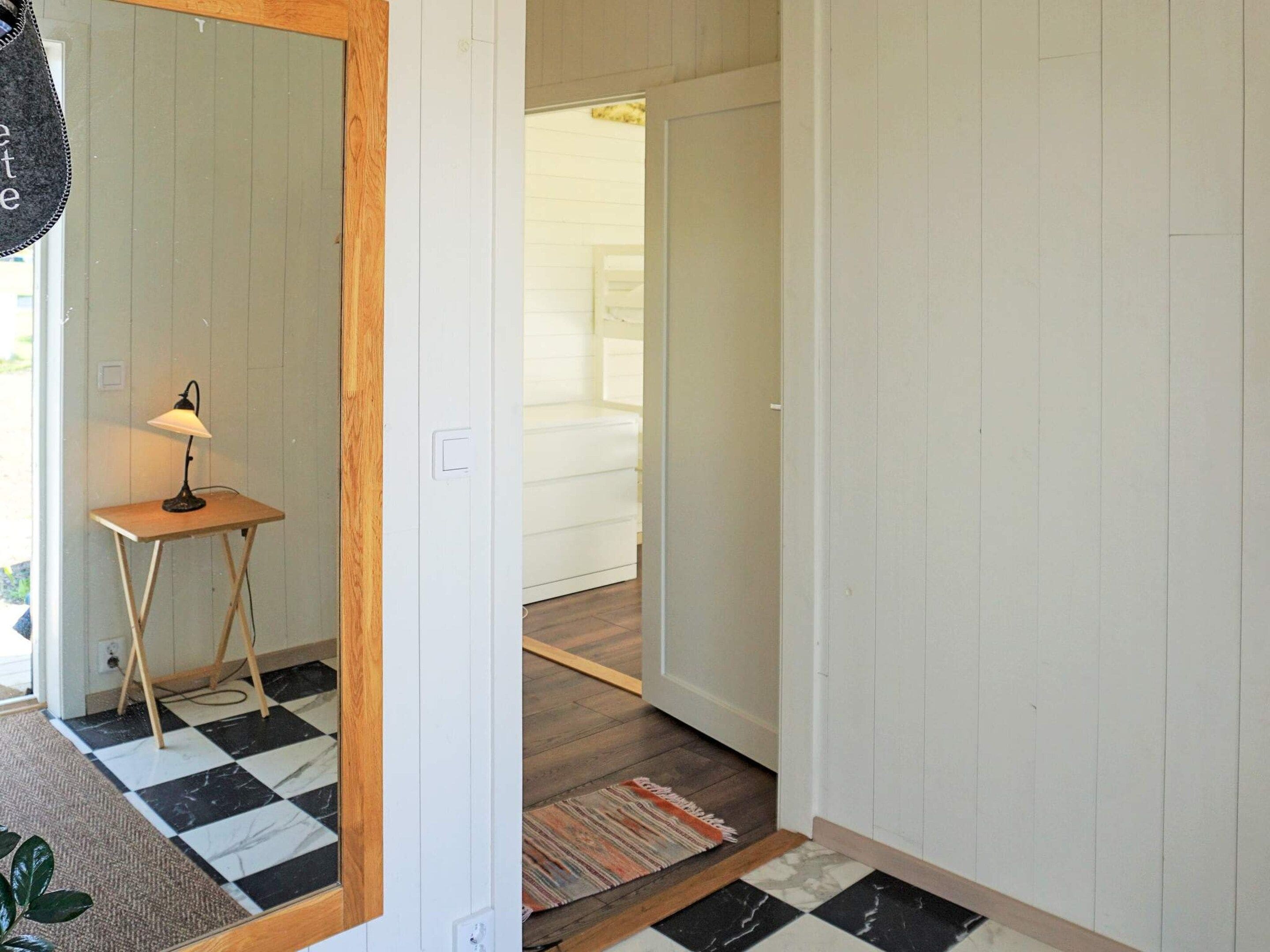 A hallway with a checkered floor, a small table with a lamp, and a mirror on the left.
