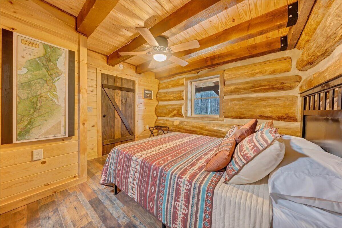 Un dormitorio tipo cabaña de madera con una cama, un ventilador de techo, un mapa en la pared y una ventana.