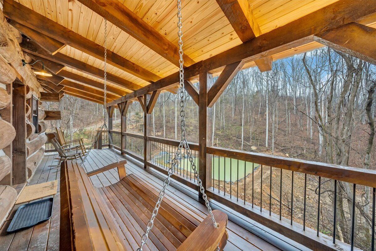 A wooden deck with a swing chair, a bench, and a view of a forested area.