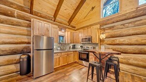 Cocina de cabaña de madera con gabinetes de madera, electrodomésticos de acero inoxidable y una zona de bar con taburetes.