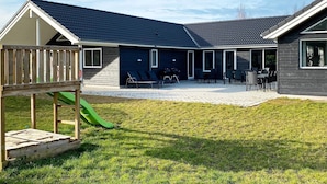 Ein modernes Gebäude mit überdachter Terrasse, Außenbestuhlung und einer Kinderspielanlage.