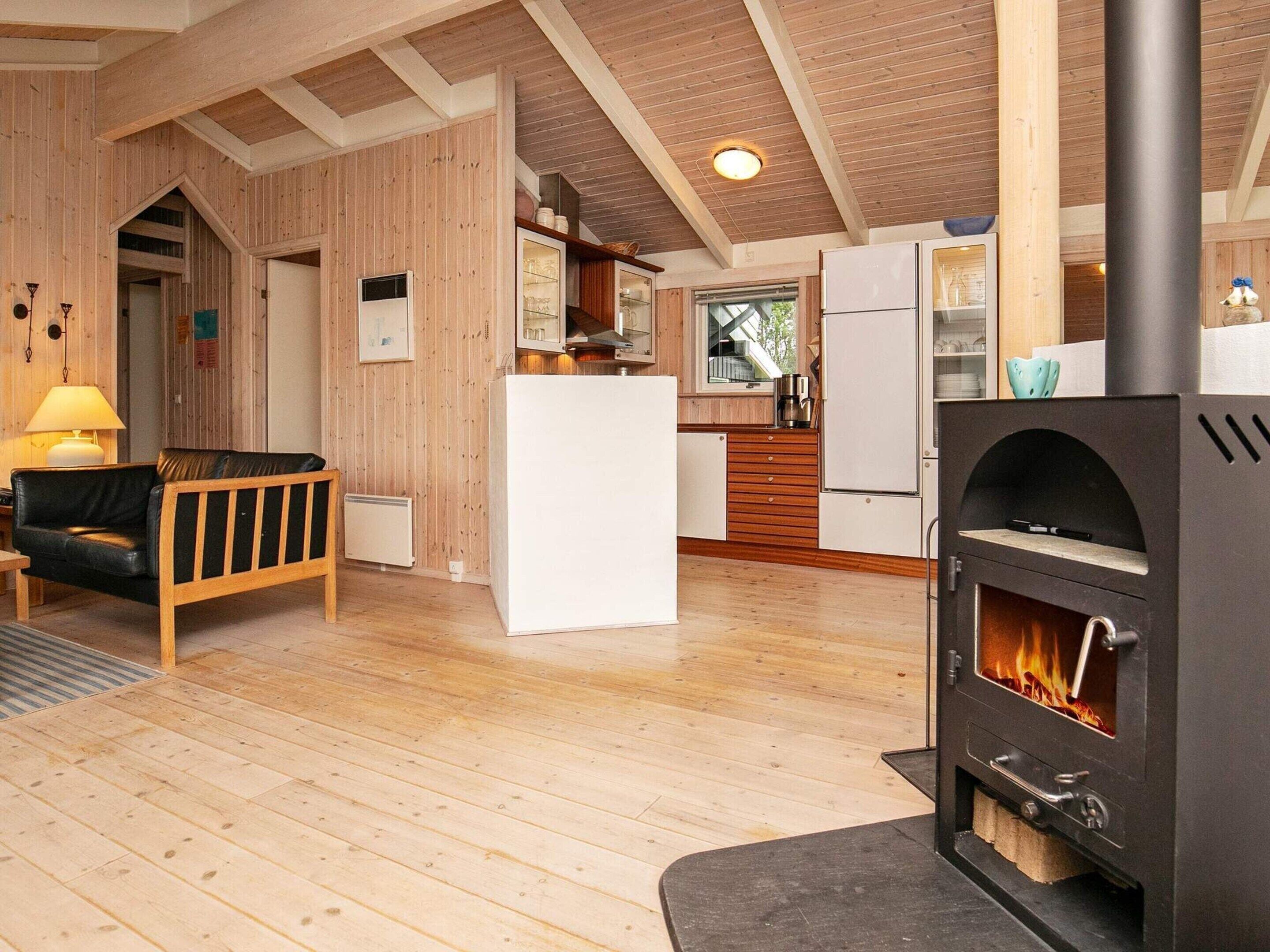 A cozy room with a wooden floor, a sofa, a white refrigerator, a kitchen area with a stove, and a wooden ceiling.