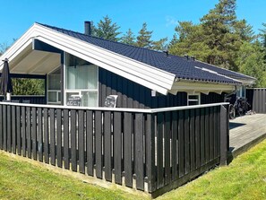 Una casa moderna con fachada oscura, techo inclinado y patio trasero cercado.
