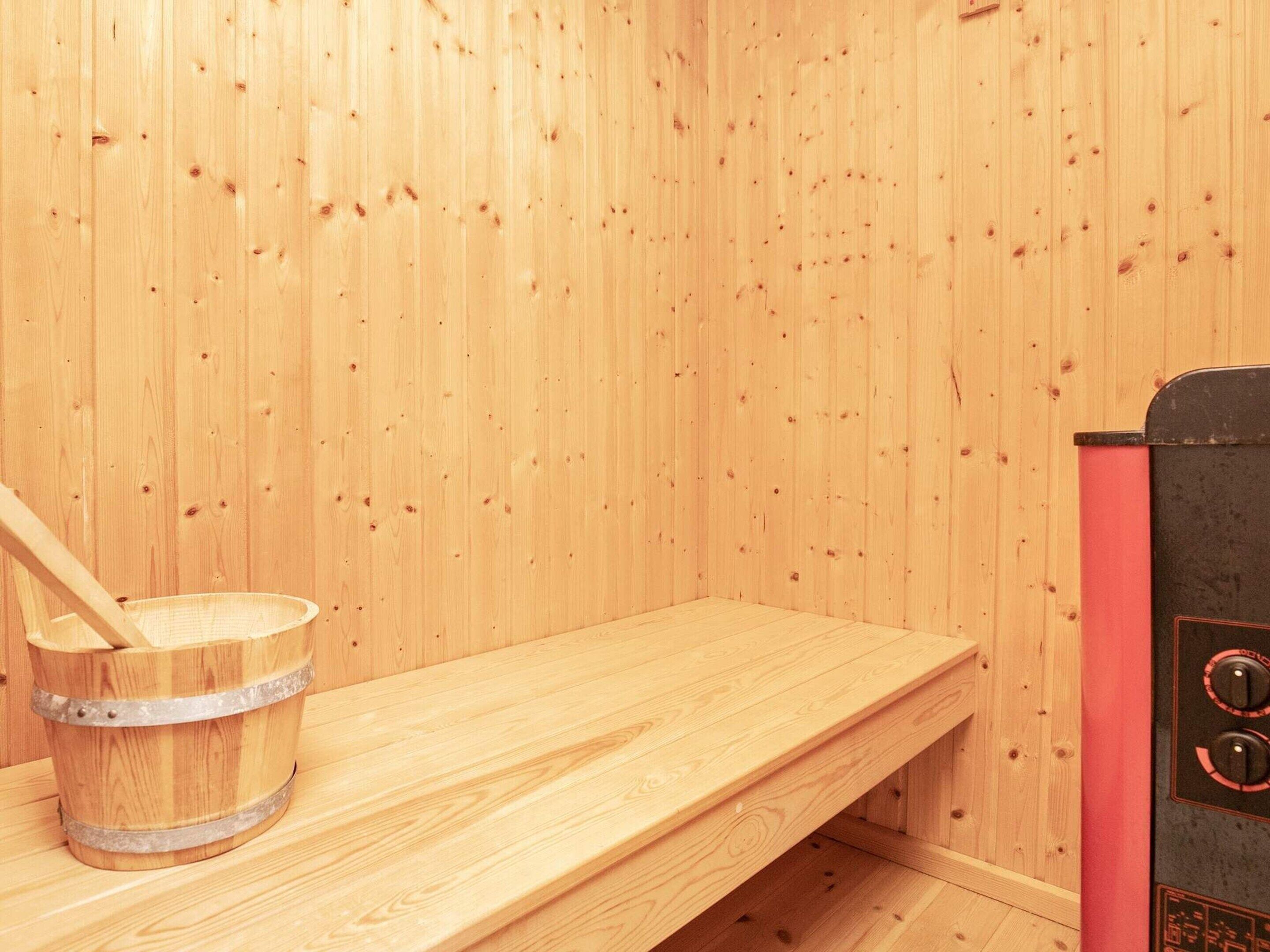 A sauna room with wooden walls, a wooden bench, and a sauna heater.