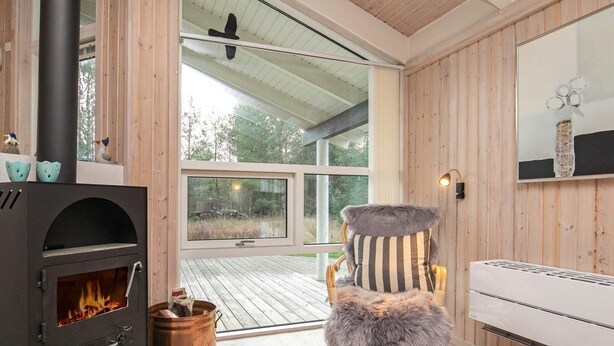Een gezellige kamer met een houtkachel, een comfortabele stoel en een groot raam met uitzicht op de natuur.