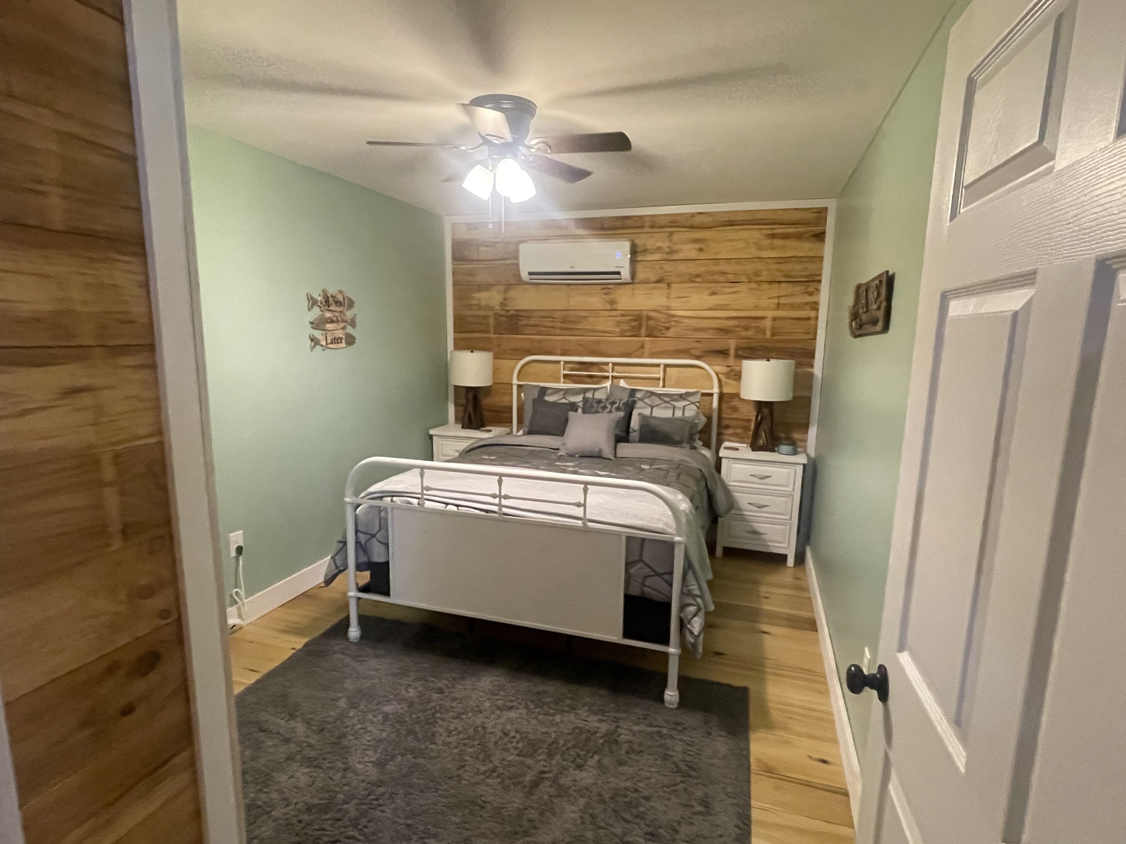 A bedroom with a bed, bedside tables, a ceiling fan, and an air conditioning unit.