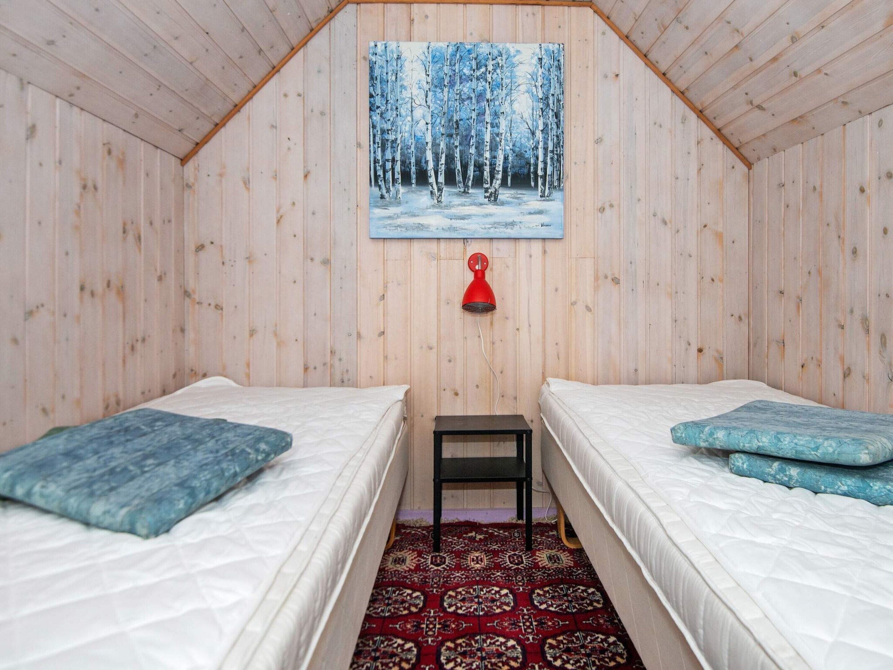 Una habitación con dos camas, una lámpara roja y un cuadro de un bosque nevado en la pared.