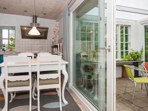 A dining area with a white table and chairs, a hanging pendant light, and a view through a glass door to an outdoor patio with chairs. - 4 Person Holiday Home in Skaerbaek (Skaerbaek)