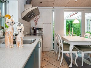 A kitchen with a built-in oven, a sink, and a dining area with a table and chairs. - 4 Person Holiday Home in Skaerbaek (Skaerbaek)
