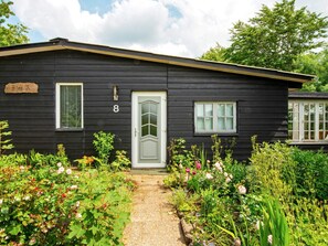 A black wooden house with a white door, number 8, and a small garden with various plants and flowers. - 4 Person Holiday Home in Skaerbaek (Skaerbaek)