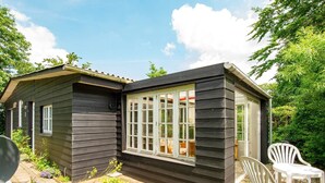 Une petite cabane en bois dotée d’une grande fenêtre, entourée de verdure et agrémentée de mobilier d’extérieur.