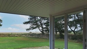 A covered patio with a table and chairs, a view of a grassy field and trees, and a clear sky. - 6 Person Holiday Home in Blavand (Blavand)