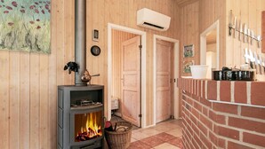 A cozy room with a wood-burning stove, a brick fireplace, wooden walls, and a door leading to another room. - 6 Person Holiday Home in Blavand (Blavand)