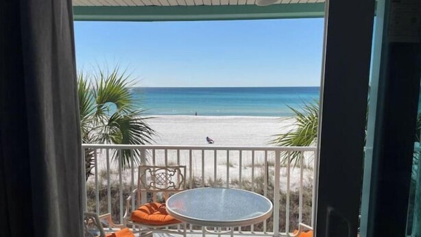 A balcony with a round table and orange cushions, overlooking a beach with sand and water. - Beachfront~ Unforgettable view! (Panama City Beach)