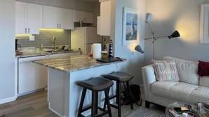 A modern kitchen with white cabinets, a central island with stools, and a dining area with a white sofa and striped pillows. - Beachfront~ Unforgettable view! (Panama City Beach)