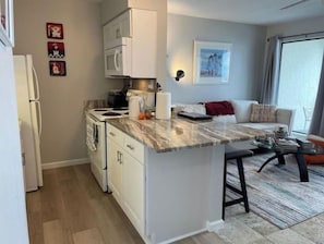 Uma cozinha compacta com eletrodomésticos brancos, bancada de mármore e um pequeno espaço de jantar com mesa e cadeiras brancas.