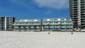A beachfront hotel with multiple balconies, a sandy beach in front, and a clear blue sky. - Beachfront~ Unforgettable view! (Panama City Beach)