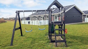 A playground with swings and a climbing structure in a grassy field. - 5 Star Holiday Home in Lokken (Lokken)