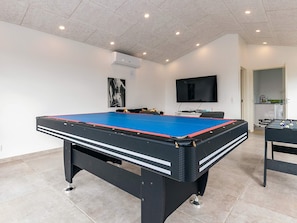 A pool table with a blue playing surface, a television mounted on the wall, and a small kitchenette area. - 5 Star Holiday Home in Lokken (Lokken)