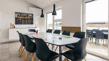 A modern meeting room with a white table, black chairs, and a cityscape painting on the wall.