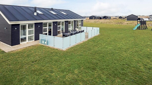 A modern building with a flat roof, large windows, and a covered outdoor seating area. - 5 Star Holiday Home in Lokken (Lokken)