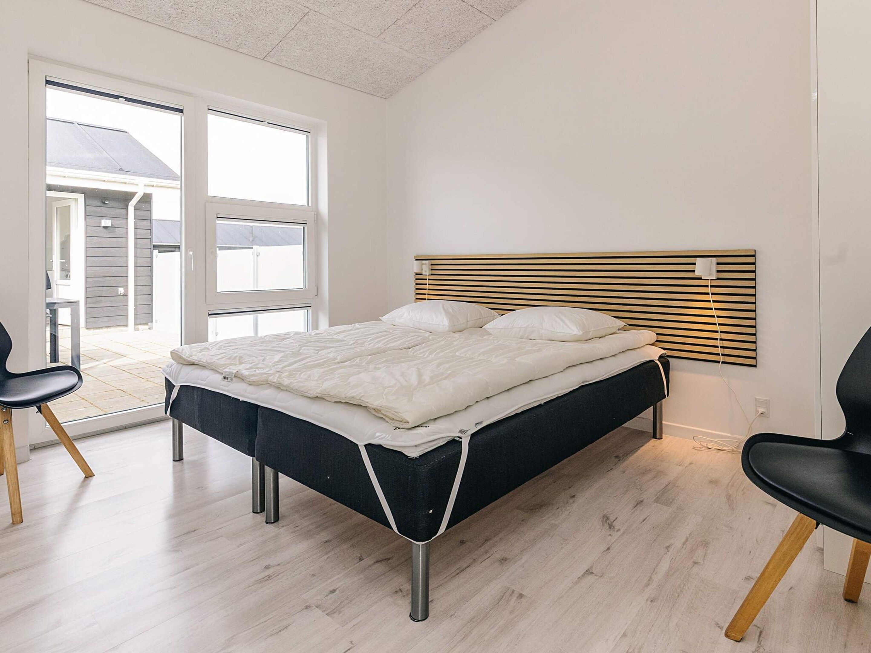 Ein Schlafzimmer mit einem Bett, zwei Stühlen, einem Fenster und Blick ins Freie.