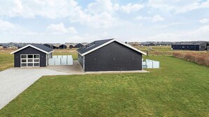 A modern building with a garage, a covered outdoor area, and a grassy field. - 5 Star Holiday Home in Lokken (Lokken)