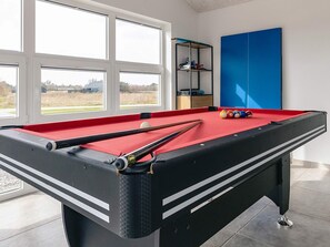 A pool table with a red felt surface, surrounded by windows with a view of a grassy field. - 5 Star Holiday Home in Lokken (Lokken)